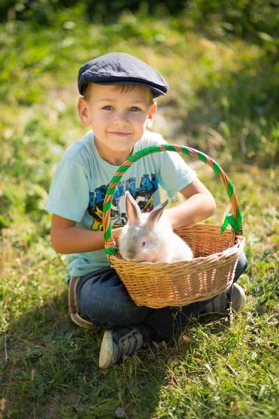 Aranyos mezőgazdasági termelő jóvágású fiú farmer élvezi a nyári nap, a falusi élet happyly mosolyogva nyúl nyuszi kosár virágokkal . — Stock Fotó