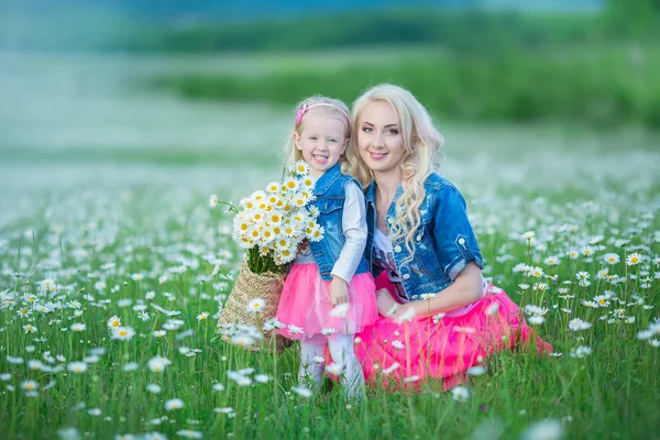 Mama i córka na piknik w polu rumianek. Dwie piękne Blondynki na sobie dżinsy kurtkę i goździk spódnica matka i dziecko dziewczynka ogarniecie w polu rumianek z koszem dandalion bukiet — Zdjęcie stockowe