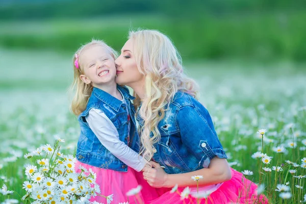 Maman et fille lors d'un pique-nique dans le champ de camomille. Deux belles blondes vêtues de jean et jupe rose Mère et bébé fille embrassant dans le champ de camomille avec panier de bouquet pissenlit — Photo