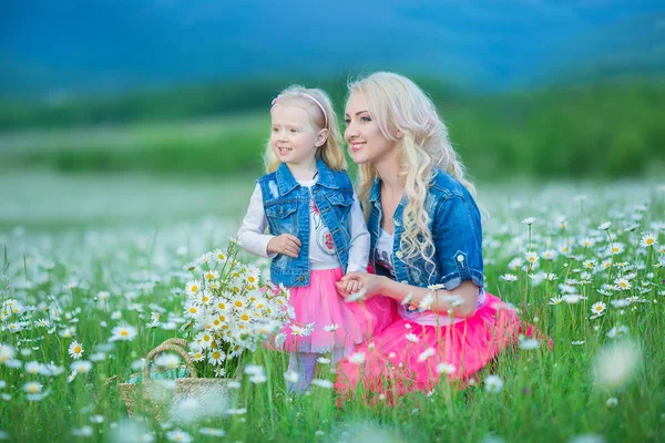 Anya és lánya, egy piknik, kamilla területén. Két gyönyörű szőke viselt farmer kabát és rózsaszín szoknya anya és a baba lány csokor dandalion kosár Kamilla területén átfogó — Stock Fotó