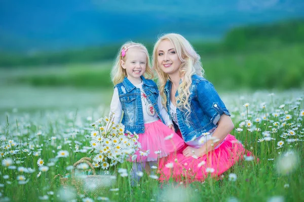 Anya és lánya, egy piknik, kamilla területén. Két gyönyörű szőke viselt farmer kabát és rózsaszín szoknya anya és a baba lány csokor dandalion kosár Kamilla területén átfogó — Stock Fotó