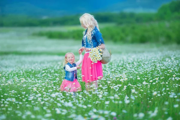 Mama i córka na piknik w polu rumianek. Dwie piękne Blondynki na sobie dżinsy kurtkę i goździk spódnica matka i dziecko dziewczynka ogarniecie w polu rumianek z koszem dandalion bukiet — Zdjęcie stockowe