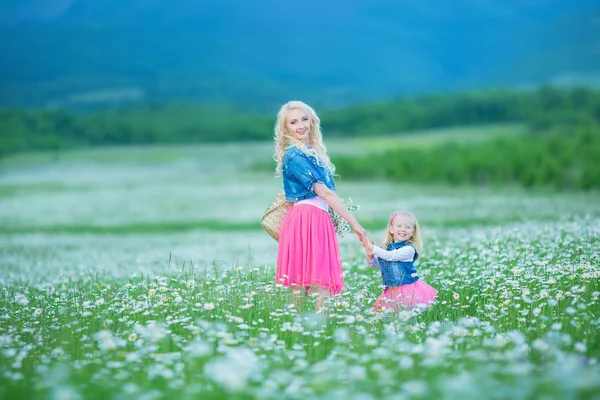 Mama i córka na piknik w polu rumianek. Dwie piękne Blondynki na sobie dżinsy kurtkę i goździk spódnica matka i dziecko dziewczynka ogarniecie w polu rumianek z koszem dandalion bukiet — Zdjęcie stockowe
