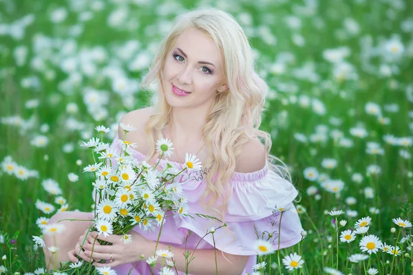 Привлекательная блондинка в ромашнем поле. Молодая женщина в венке в окружении ромашки в стильном розовом платье наслаждаясь летней весной — стоковое фото