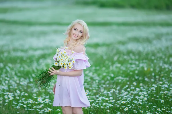 Привлекательная блондинка в ромашнем поле. Молодая женщина в венке в окружении ромашки в стильном розовом платье наслаждаясь летней весной — стоковое фото