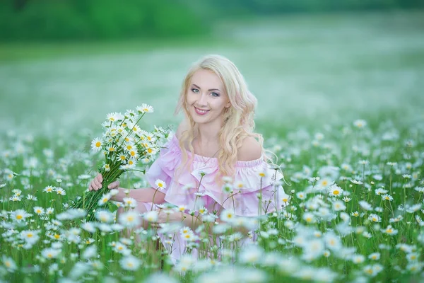 Attraktive Blondine im Kamillenfeld. junge Frau im Kranz umgeben von Kamillen in elegantem rosa Kleid genießt den sommerlichen Frühling — Stockfoto