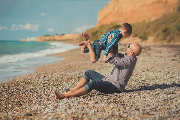 Weekend na plaży tata i syn, siedząc na plaży i patrząc na siebie nawzajem. Plaża Stone sea pianki rodowód — Zdjęcie stockowe