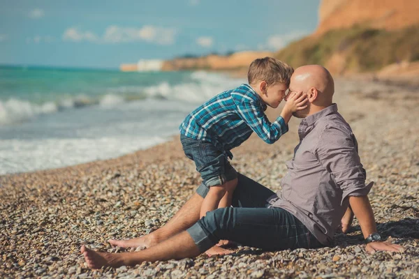 Weekend na plaży tata i syn, siedząc na plaży i patrząc na siebie nawzajem. Plaża Stone sea pianki rodowód — Zdjęcie stockowe