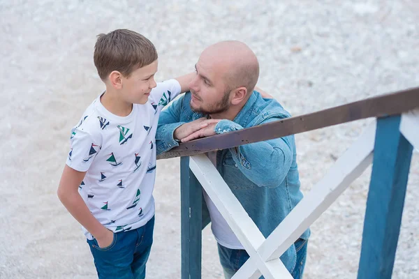 Guapo audaz elegante vestido en jeans hombre en gorra azul sentado en un lado del mar de playa junto con lindo hijo adolescente andpretty bulldog inglés . — Foto de Stock