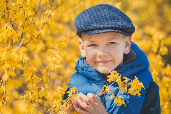 Netter hübscher Junge in stylischem blauem Kleid und Hut in der Nähe gelber Blumen und genießt den Frühling — Stockfoto