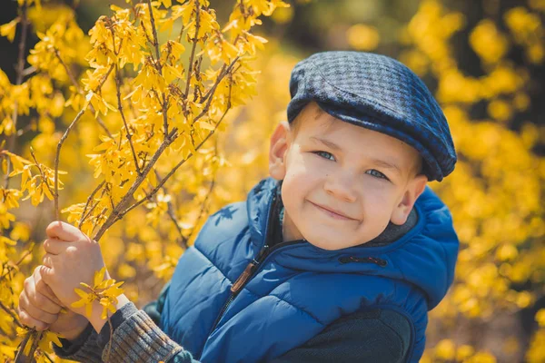 Netter hübscher Junge in stylischem blauem Kleid und Hut in der Nähe gelber Blumen und genießt den Frühling — Stockfoto