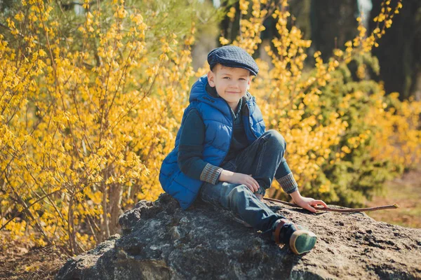 Netter hübscher Junge in stylischem blauem Kleid und Hut in der Nähe gelber Blumen und genießt den Frühling — Stockfoto