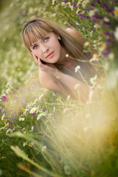 Beautiful woman enjoying daisy field, nice female lying down in meadow of flowers, pretty girl relaxing outdoor, having fun, holding plant, happy young lady and spring green nature, harmony concept Stock Photo