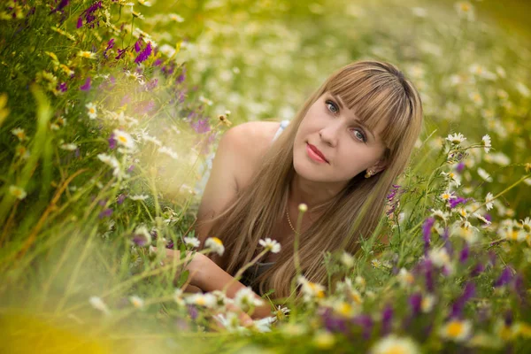 Mulher bonita desfrutando de campo de margarida, fêmea agradável deitado no prado de flores, menina bonita relaxante ao ar livre, se divertindo, segurando planta, jovem senhora feliz e natureza verde primavera, conceito de harmonia Imagens Royalty-Free