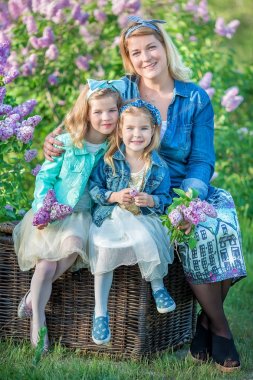 İki sevimli gülümseyen kız kız kardeş güzel birlikte leylak alan ile anne kadın bush tüm şık elbiseler ve kot ceket giyiyor.