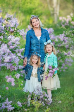 İki sevimli gülümseyen kız kız kardeş güzel birlikte leylak alan ile anne kadın bush tüm şık elbiseler ve kot ceket giyiyor.