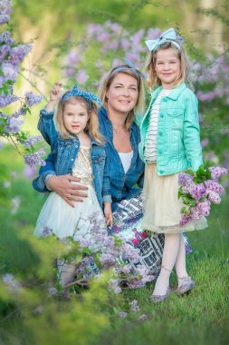 İki sevimli gülümseyen kız kız kardeş güzel birlikte leylak alan ile anne kadın bush tüm şık elbiseler ve kot ceket giyiyor.
