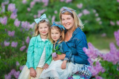 İki sevimli gülümseyen kız kız kardeş güzel birlikte leylak alan ile anne kadın bush tüm şık elbiseler ve kot ceket giyiyor.