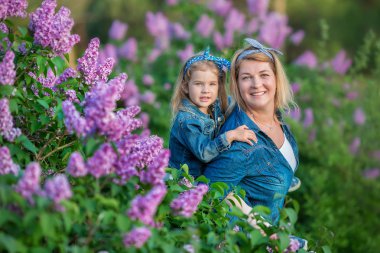 İki sevimli gülümseyen kız kız kardeş güzel birlikte leylak alan ile anne kadın bush tüm şık elbiseler ve kot ceket giyiyor.