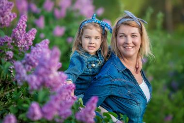 İki sevimli gülümseyen kız kız kardeş güzel birlikte leylak alan ile anne kadın bush tüm şık elbiseler ve kot ceket giyiyor.