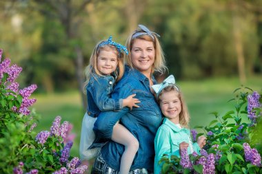 İki sevimli gülümseyen kız kız kardeş güzel birlikte leylak alan ile anne kadın bush tüm şık elbiseler ve kot ceket giyiyor.