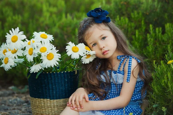 Jeune fille mignonne en jeans robe debout près de fleurs jaunes avec panier plein de camomille . — Photo