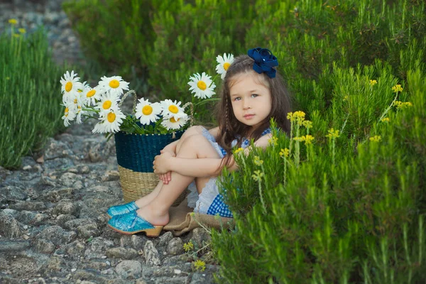 Jeune fille mignonne en jeans robe debout près de fleurs jaunes avec panier plein de camomille . — Photo