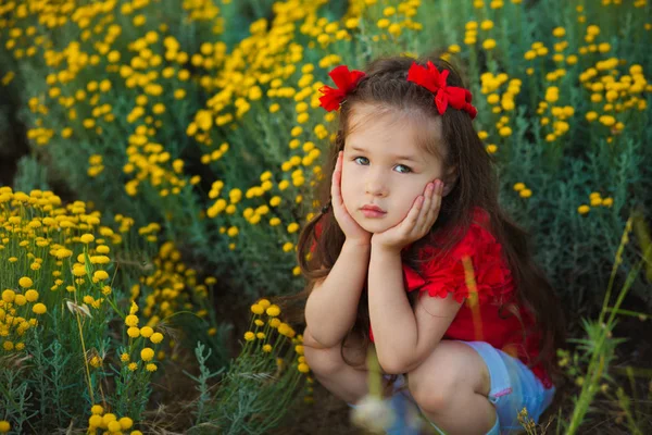 Jeune fille mignonne en chemise rouge et short blanc debout près de fleurs jaunes . — Photo