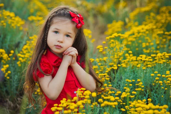 Jeune fille mignonne en chemise rouge et short blanc debout près de fleurs jaunes . — Photo