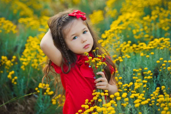 Giovane ragazza carina in camicia rossa e pantaloncini bianchi in piedi vicino a fiori gialli . — Foto Stock