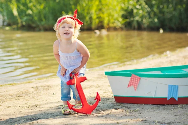 A cute little girl in a red bathing suit standing on the beach against the backdrop of boats — Stock Photo, Image
