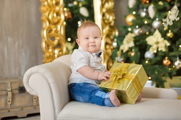 O lindo menino celebra o Natal. Férias de Ano Novo. Bebê em um traje de Natal roupas casuais com presentes na pele perto da árvore de ano novo em decorações de estúdio . — Fotografia de Stock