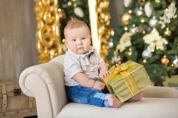 O lindo menino celebra o Natal. Férias de Ano Novo. Bebê em um traje de Natal roupas casuais com presentes na pele perto da árvore de ano novo em decorações de estúdio . — Fotografia de Stock