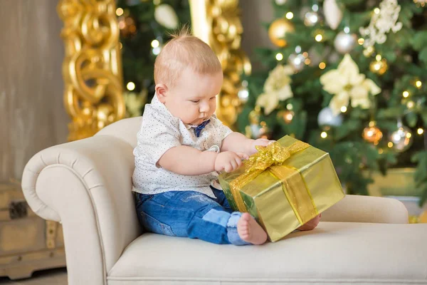 Hermoso niño pequeño celebra la Navidad. Vacaciones de Año Nuevo. Bebé en un traje de Navidad ropa casual con regalos en piel cerca del árbol de año nuevo en decoraciones de estudio . — Foto de Stock
