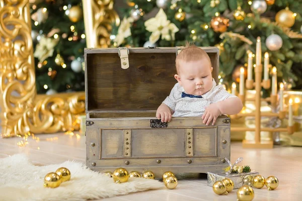 Beautiful little baby boy celebrates Christmas. New Year's holidays. Baby in a Christmas costume casual clothes with gifts on fur close to new year tree in studio decorations.