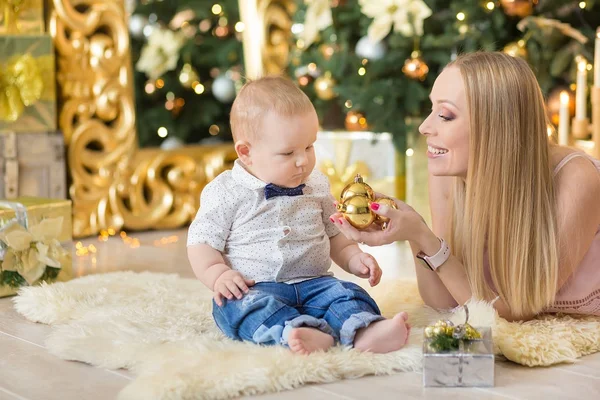 Mãe de família feliz e bebê pequeno filho jogando em casa nas férias de Natal. Criança com a mãe no quarto festivamente decorado com árvore de Natal. Retrato de mãe e bebê menino em roupas casuais — Fotografia de Stock