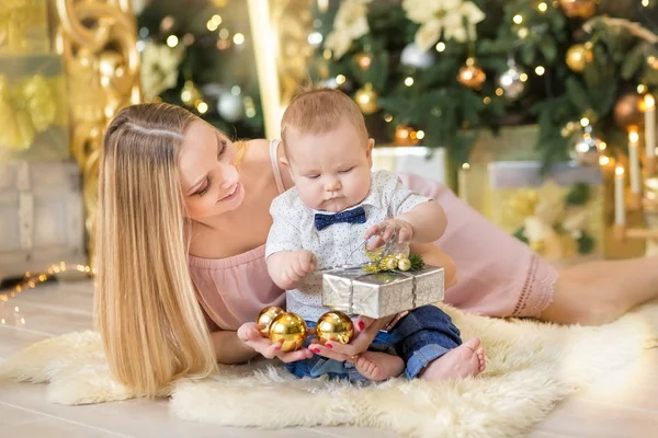 Mãe de família feliz e bebê pequeno filho jogando em casa nas férias de Natal. Criança com a mãe no quarto festivamente decorado com árvore de Natal. Retrato de mãe e bebê menino em roupas casuais — Fotografia de Stock