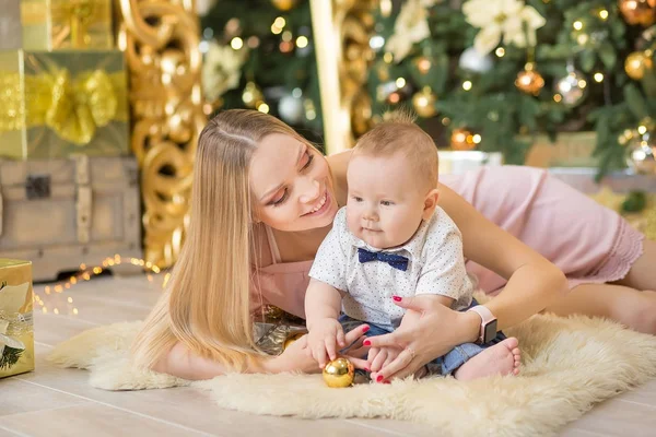 Lycklig familj mamma och baby lille son spelar hem på jullov. Småbarn med mamma i festligt dekorerade rum med julgran. Porträtt av mor och baby boy i casual kläder — Stockfoto
