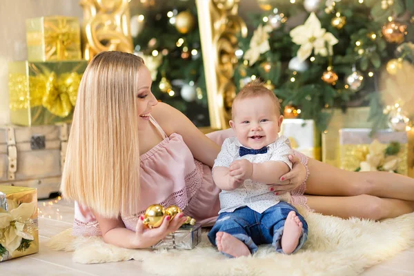 Mãe de família feliz e bebê pequeno filho jogando em casa nas férias de Natal. Criança com a mãe no quarto festivamente decorado com árvore de Natal. Retrato de mãe e bebê menino em roupas casuais — Fotografia de Stock