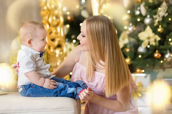 Mãe de família feliz e bebê pequeno filho jogando em casa nas férias de Natal. Criança com a mãe no quarto festivamente decorado com árvore de Natal. Retrato de mãe e bebê menino em roupas casuais — Fotografia de Stock