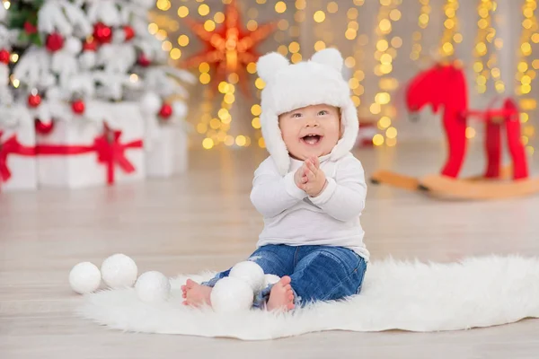 Beautiful little baby boy celebrates Christmas. New Year's holidays. Baby in a Christmas costume casual clothes with gifts on fur close to new year tree in studio decorations.