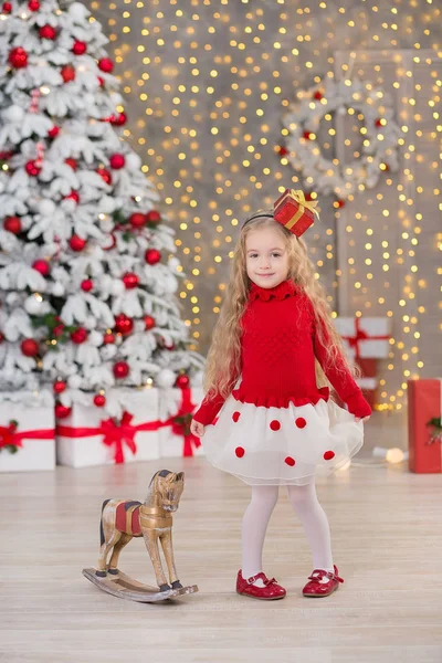 Mooi meisje glimlachend, zittend in de buurt van enorme gouden spiegel genoeg presenteert op bont kerst groen wit luxe boom decoraties en beneden liggen geschenken — Stockfoto