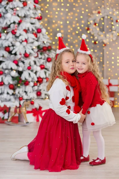 两个美的圣诞肖像可爱的女孩微笑的姐妹朋友和圣诞节豪华的绿色白树在独特的室内工作室与巨大的金色镜子和毛皮 免版税图库图片