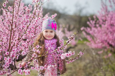 Bahar genç şeftali ağacına sahasında bahar sezonunda pembe giymiş pembe flowers.smiling kızla şirin güzel şık giyinmiş sarışın kız ayakta.