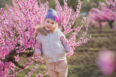 Bahar genç şeftali ağacına sahasında bahar sezonunda pembe giymiş pembe flowers.smiling kızla şirin güzel şık giyinmiş sarışın kız ayakta.