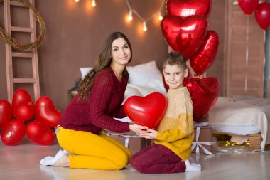 Beautiful cute young brunette mom mother with her teenager handsome boy holding each other and happy together.Woman in yellow pens and red sweeter. clipart