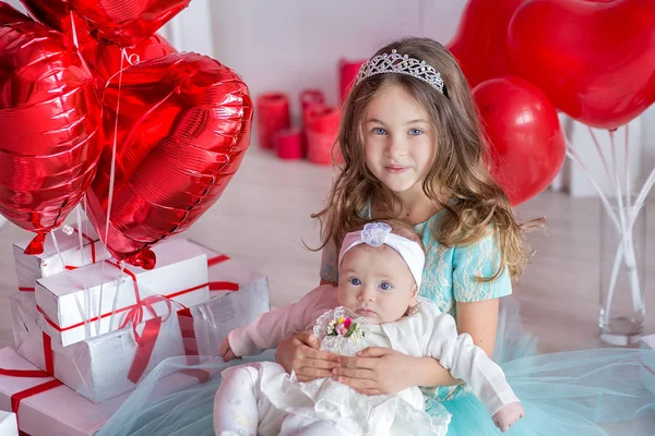Cute baby girl celebrating birth day together close to red balloons.Lovely scene of baby on sofa divan with presents and red baloons.