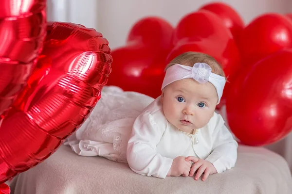 Cute baby girl celebrating birth day together close to red balloons.Lovely scene of baby on sofa divan with presents and red baloons.