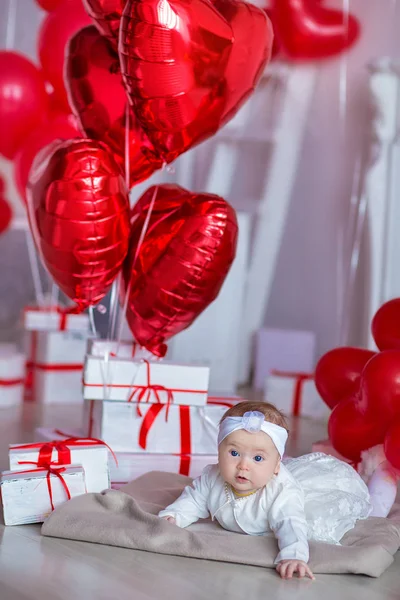 Dziewczyna słodkie dziecko obchodzi dzień urodzenia razem blisko czerwone balony. Piękne sceny dziecka na kanapie divan z prezentami i czerwone balony. — Zdjęcie stockowe