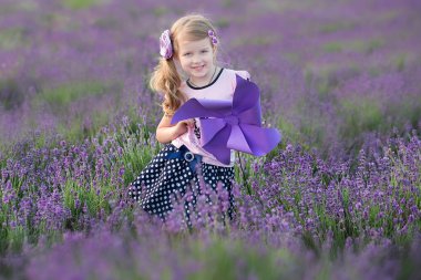 Lavanta sahada gülümseyen genç kızı ile genç anne. Kızı anne eller üzerinde oturuyor. Renkli elbise ve koyu mavi elbiseli anne kız.